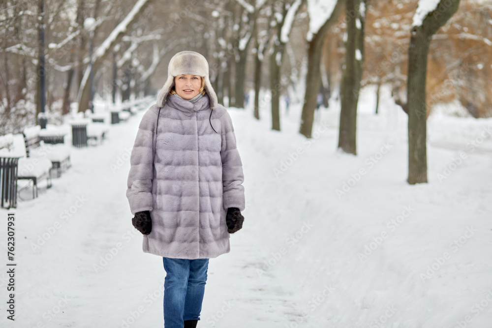 Woman in fur coat and hat walks in winter park.