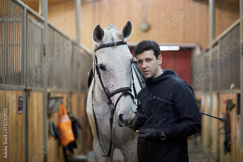 Man holds horse by bridle in riding stables.