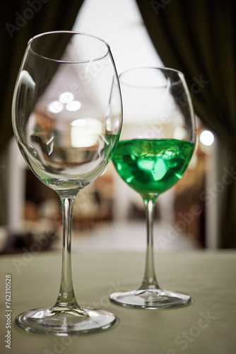 Empty wineglass and another one with green beverage on table in cafe.