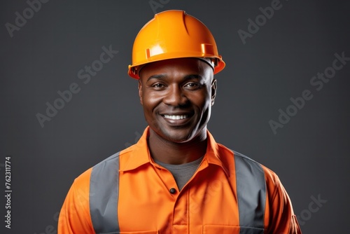 Happy African American builder An engineer in an orange uniform and helmet stands confidently on a gray background.