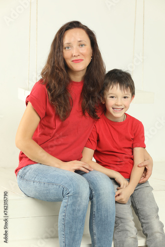 Woman and her little son in jeans and red t-shirts pose in white studio and smile