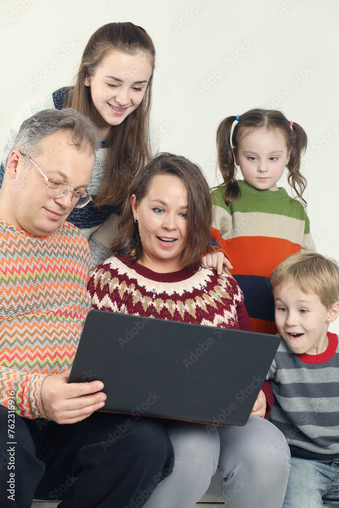 Father, mother, son, two daughter in sweaters look into laptop in white studio Father, mother, son, two daughter in sweaters look into laptop in white studio