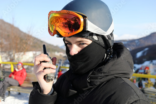 Boy with ski goggles saids on radio in ski resort at winter sunny day photo