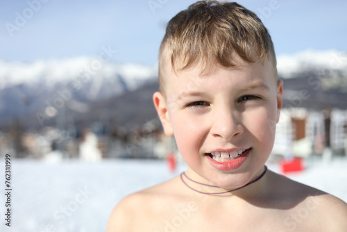 Happy half-naked boy poses at ski resort at winter day among mountains photo