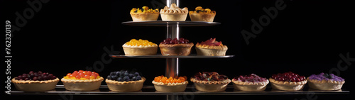 An assortment of pies with various colorful fruit toppings arranged on a metal shelf against a black background.