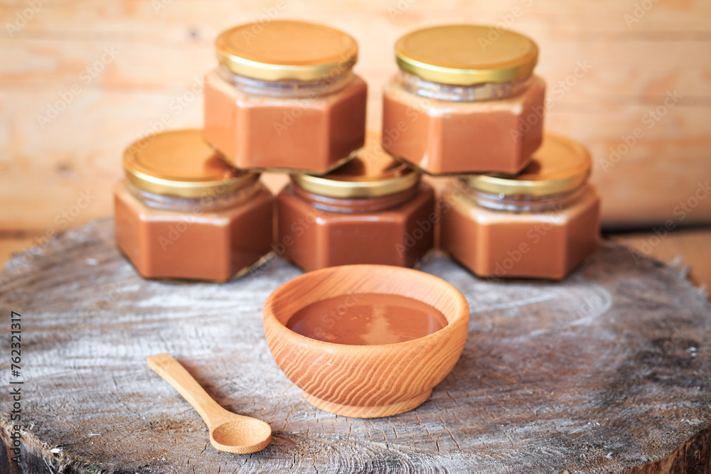 Boiled condensed milk in a wooden plate, close-up against the background of glass jars filled with condensed milk, food photography, wooden background. Boiled condensed milk in a wooden plate, close-up against the background of glass jars filled with condensed milk, food photography, wooden background.