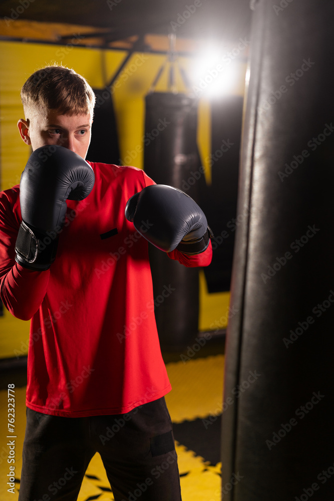 Young boxing male athlete punching boxing bag while exercising in gym during intense workout.