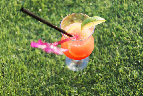 Bright fruit cocktail with piece of lime and straw on green lawn