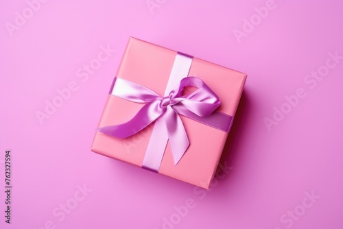 A pink gift box tied with a luxurious purple satin ribbon on a lavender background, symbolizing thoughtfulness and celebration. © Anatolii