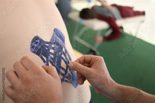 Physiotherapist hands glues emplastrum for patient in clinic of kinesiotherapy, closeup, other patient out of focus