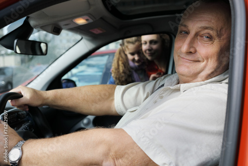 Elderly man fastened sits in car, woman, girl look into window, focus on man