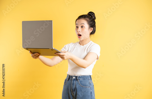 Portrait of Asian woman using computer and posing on yellow background