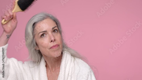 A beautiful woman with gray hair combs her hair on a pink background