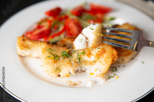Baked whitefish fillet with creamy sauce served on plate with vegetables and greens.