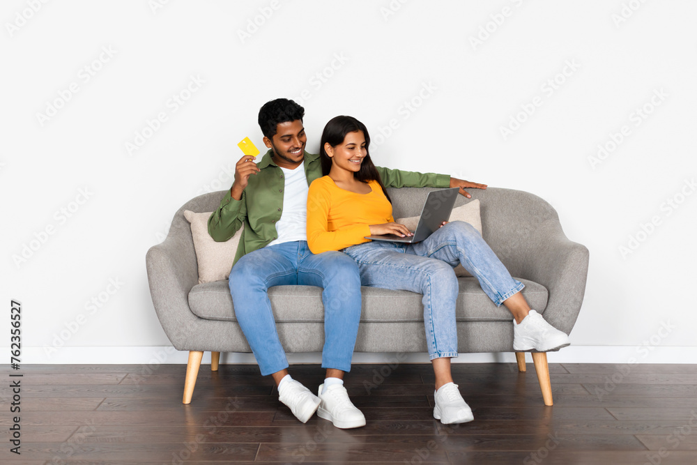 Engaged indian couple with credit card and laptop on couch Engaged indian couple with credit card and laptop on couch