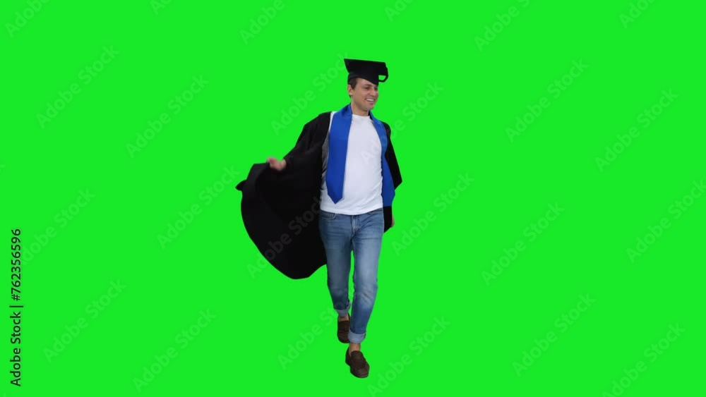 Young and happy university graduate wearing gown walking and emotionally dancing on green background Young and happy university graduate wearing gown walking and emotionally dancing on green background