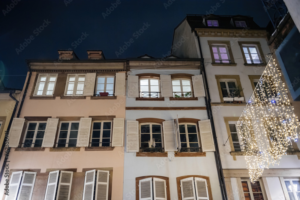Fototapeta premium Residential building facade at night with windows lit and festive lights in the foreground
