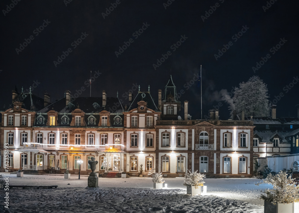 Snow-covered grounds of a majestic historical building illuminated under a clear night sky