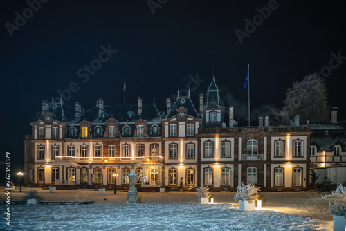 Front view of a grand historical manor chateau de Pourtales, adorned with festive lights on a snowy evening