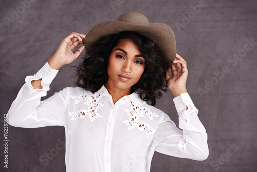 Portrait, studio and woman with cowboy fashion, confidence and relax with girl in stetson hat. Rodeo, western style and face Mexican model with cowgirl culture, wild west clothes and grey background photo