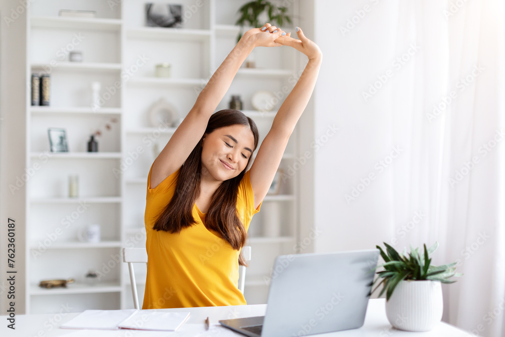 Happy asian woman stretching with her arms raised, taking break at her home office Happy asian woman stretching with her arms raised, taking break at her home office