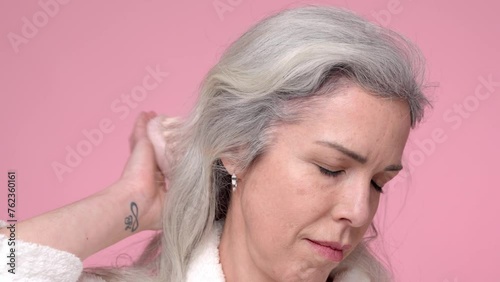 A woman with gray hair is massaging her hair, smiling, against a pink background