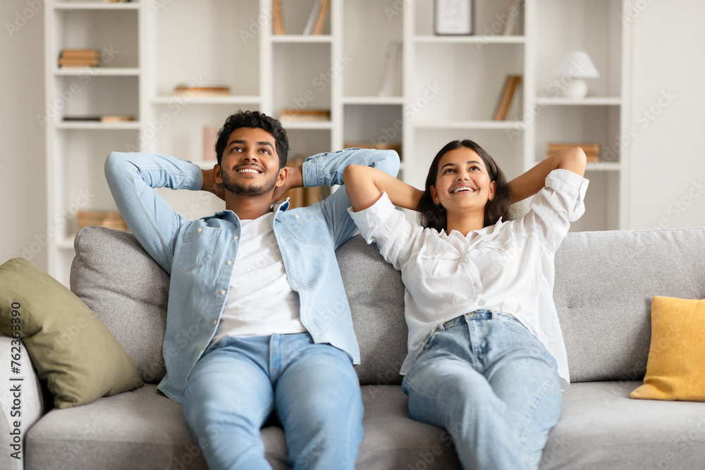 Content indian couple relaxing on sofa with hands behind head Content indian couple relaxing on sofa with hands behind head