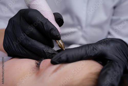 In the hands of the master of permanent makeup tattoo machine with which he performs the work. PMU Procedure  Permanent Eyebrow Makeup.