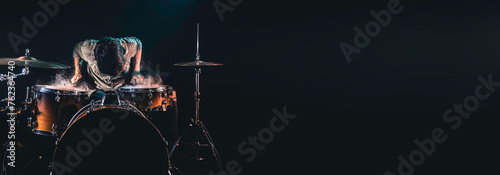 Professional drummer playing on drum set on stage on the black background.
