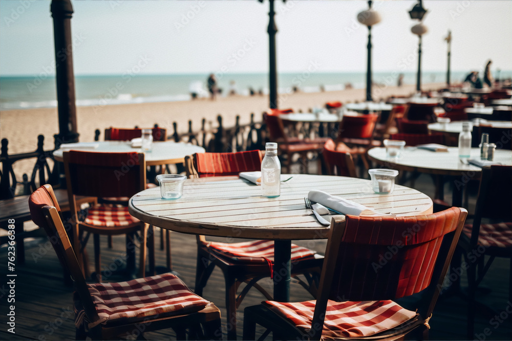 Naklejka premium An empty restaurant table with a water bottle and glass on the beach with a blurred background of the ocean and a few people walking.