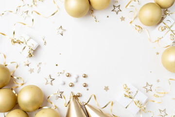 Fashion birthday party festive background with golden decoration from balloons, carnival cap, gift box and confetti stars on white table top view.