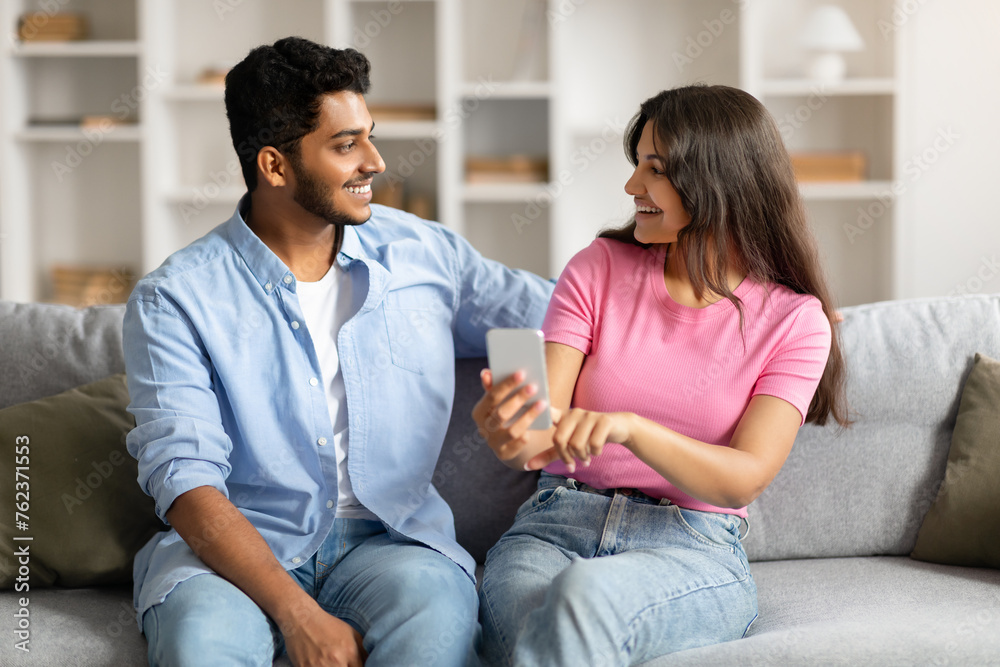 Hindu couple on couch sharing phone, both smiling Hindu couple on couch sharing phone, both smiling