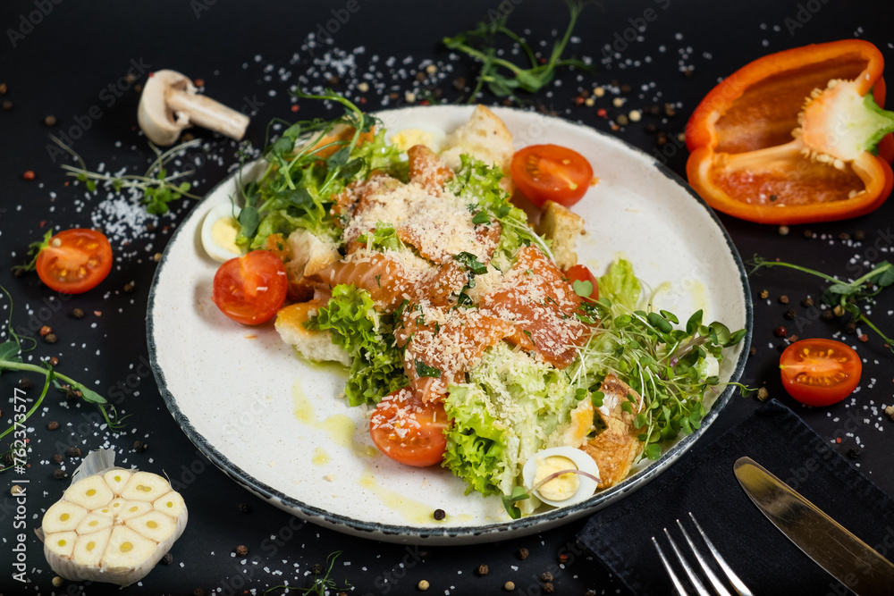 Classic Caesar salad with salmon. On a black stone background. In a plate, close-up. Classic Caesar salad with salmon. On a black stone background. In a plate, close-up.