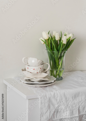 A bouquet of tulips in a glass vase and retro-style ceramic tableware on a white chest of drawers