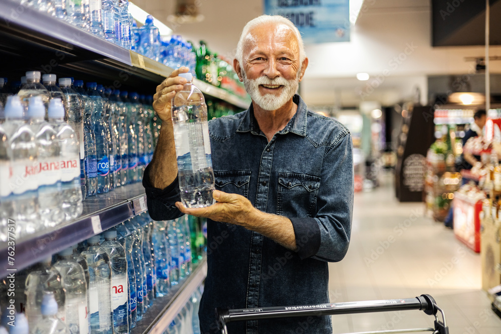 Man in supermarket, grocery store customer. Male buyer shopping groceries in supermarket from shelf standing with shop cart.