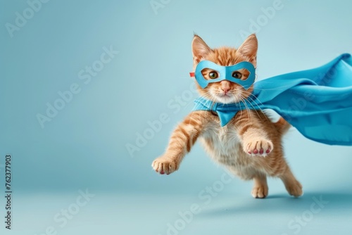 Superhero cat, Cute orange tabby kitty with a blue cloak and mask jumping and flying on light blue background with copy space. 