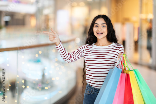 Positive young indian woman carrying purchases, copy space