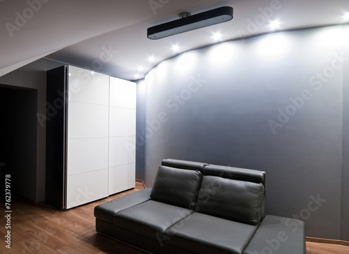 Modern bedroom, simplistic style with brown leather sofa and wall lighting. Contemporary youth room design.