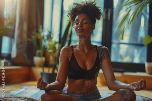 wellness yoga meditation concept, A woman is sitting on the floor. She is wearing a black tank top and blue shorts. The room is decorated with plants and has a calming atmosphere © BrightSpace