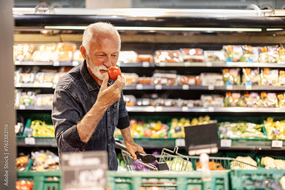 Mature man shopping for fruit And vegetables in a supermarket. Man defining quality of tomato in supermarket