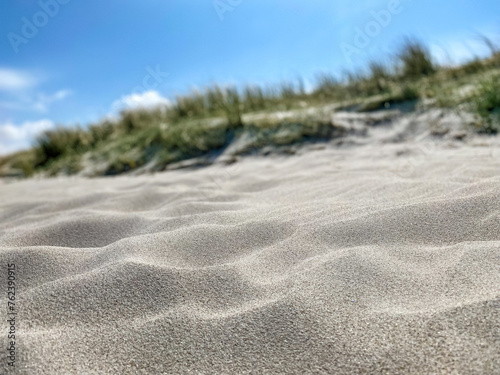 Close-Up/Nahaufnahme eines Sandstrandes mit begrünter Dünung und blauem Himmel im unscharfen Hintergrund, flache Tiefenschärfe