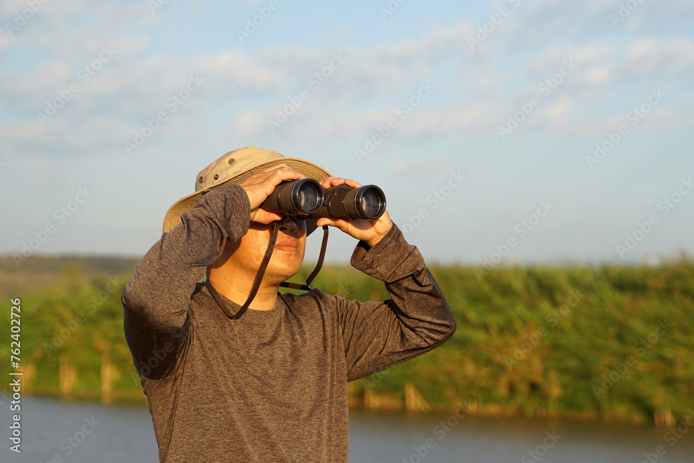Asian man uses binoculars to observe local birds along a river. Soft and selective focus. Asian man uses binoculars to observe local birds along a river. Soft and selective focus.