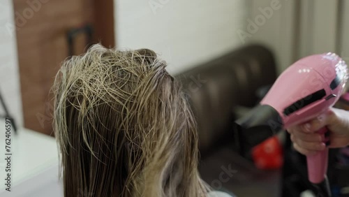 close-up of a haircut in a beauty salon, the master dries hair with a hair dryer after cutting beautiful long blond long hair
