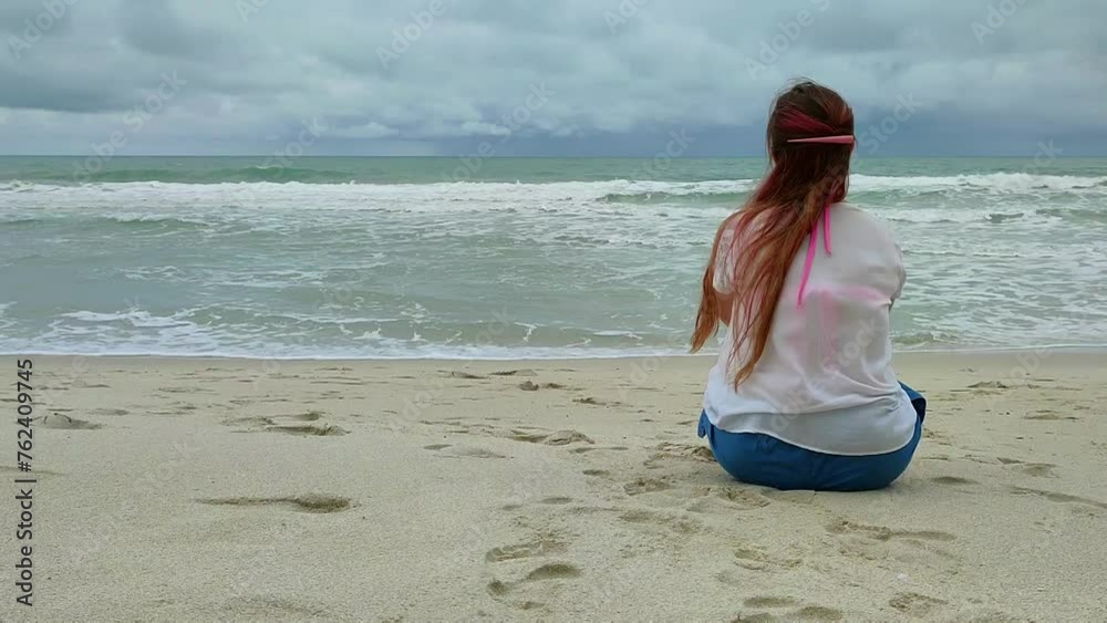 Young woman sitting on the beach looking at the sea. Alone woman ...