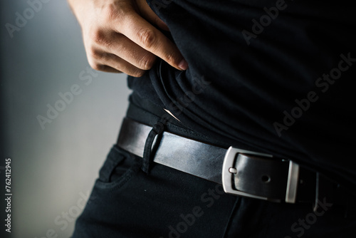 the waist of a man dressed in a black T-shirt and trousers and accented by a black leather belt