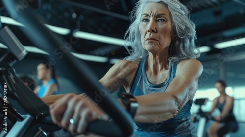Senior Woman Focused on Gym Workout, dedicated elderly woman with grey hair intensely working out on a gym bike, showcasing health and activity in older age