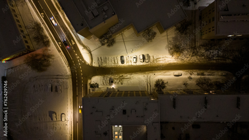 Drone photography of a street between buildings covered by snow during winter night Drone photography of a street between buildings covered by snow during winter night