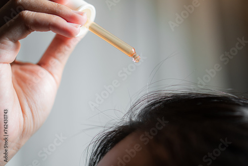 The girl puts on her black hair of hydrolyte from a pipette hair tonic