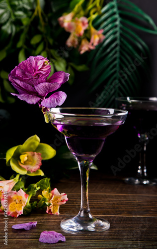 Cold purple violet exotic cocktail in glass with decorated flowers and petals. Tropical vibes.
