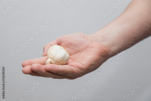 A Caucasian man holds raw white garlic in a hand.